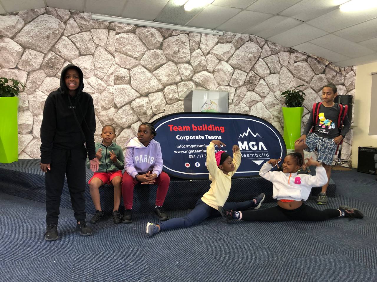 Young participants gathered beside MGA branding during an indoor programme